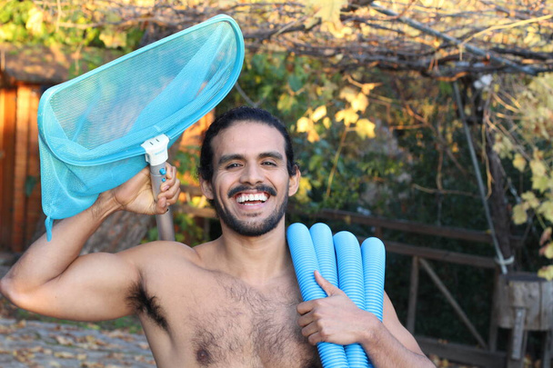 retrato de primer plano del joven guapo con bigote y pelo largo sosteniendo red y tubería para la limpieza de la piscina - Foto, Imagen