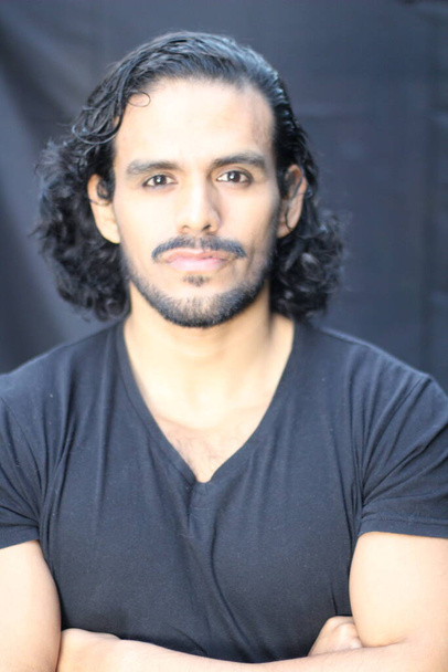 close-up portrait of handsome young man with mustache and long hair in black t-shirt in front of black wall - Foto, Imagem