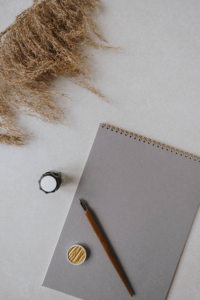 Flatlay blank paper sheet pad, pampas grass, fountain pen, golden ink on beige concrete background. Home office desk workspace. Business, work, lettering, handwriting template. Flat lay, top view. - Photo, Image