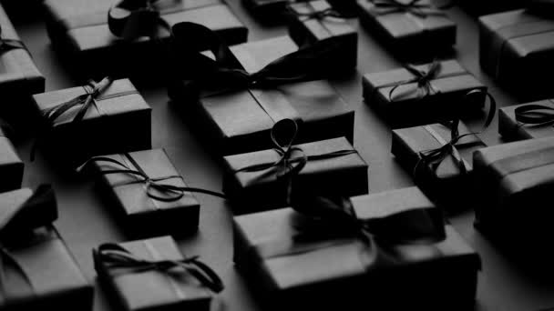 Donker kerstthema. Vierkante doos geschenken verpakt in zwart papier en lint gerangschikt op zwart - Video