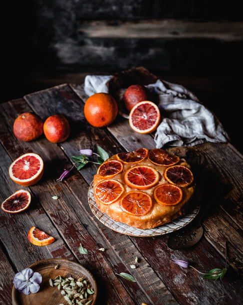 blood orange pie on wooden table with fresh oranges, spices and textile - Fotó, kép