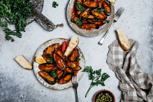 mussels in tomato sauce with fresh herbs and toasted baguette on grey background, top view, comfort food concept - Foto, imagen