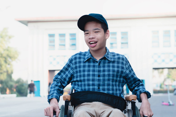 Азиатский специальный ребенок на инвалидном кресле в голубой рубашке и кепке с рюкзаком научится пользоваться инвалидными колясками на улице, стиль жизни в возрасте образования детей-инвалидов, счастливая концепция ребенка-инвалида. - Фото, изображение