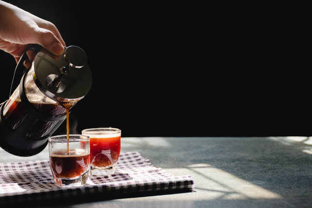 Two shot glass from French press coffee maker on the old wood table and black background and sunlight in the morning by window, Coffee Time or business break concept. - 写真・画像