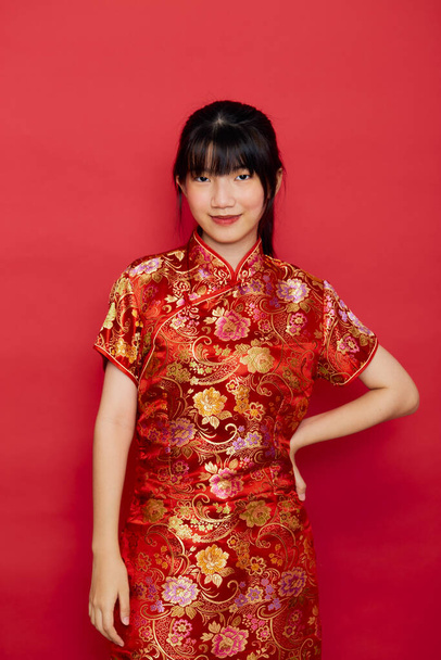 Schattig jong aziatisch vrouw dragen cheongsam met actie voor Chinees nieuwjaar concept op een rode achtergrond - Foto, afbeelding