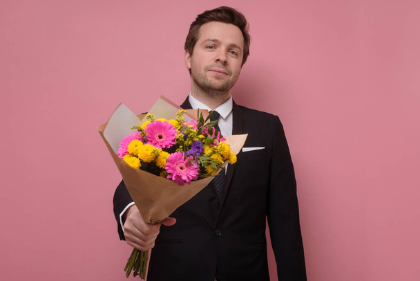 Uśmiechnięty mężczyzna trzymający bukiet kwiatów składający propozycję. - Zdjęcie, obraz