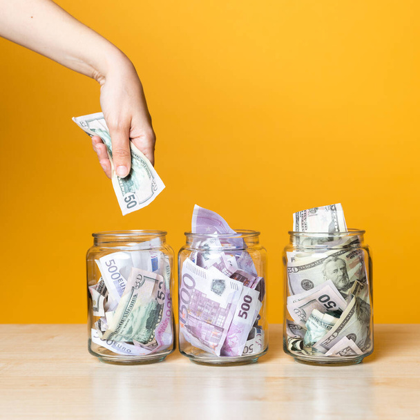 Multi-currency accounts, concept. Dollars and euros in a glass jar on a bright yellow background - Foto, imagen
