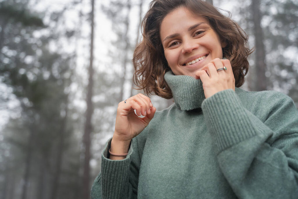 Happy woman in warm cozy green sweater in beautiful foggy pine forest - Photo, image