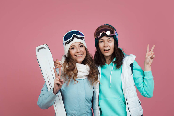Two funny friends in winter clothes on a pink background. Two skiers - Foto, Imagem