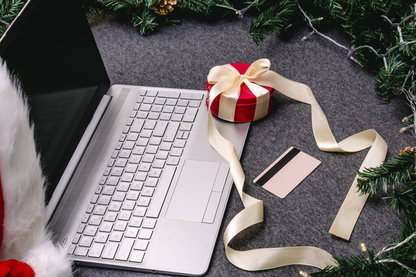 Christmas shopping online with a credit card for the holiday. Laptop with gifts on the table next to fir branches and a garland of lights. - 写真・画像