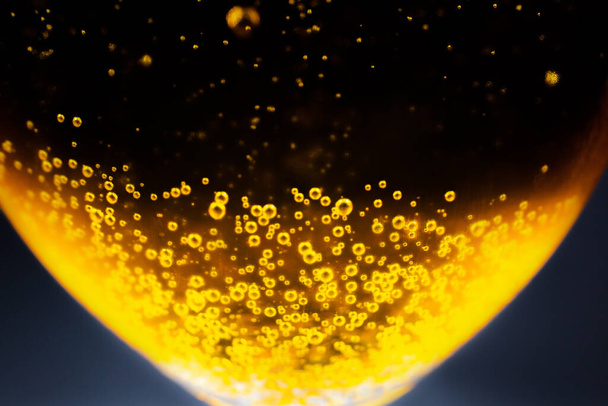 Nestemäinen kullankeltainen bensiini kuplia tausta olutta tai samppanjaa lasi. Lähemmäs, makroheitto. Pehmeä fokuskuva. - Valokuva, kuva