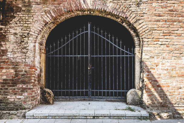 A closeup shot of a locked gate with an arch-shaped brick wall entrance - Fotó, kép