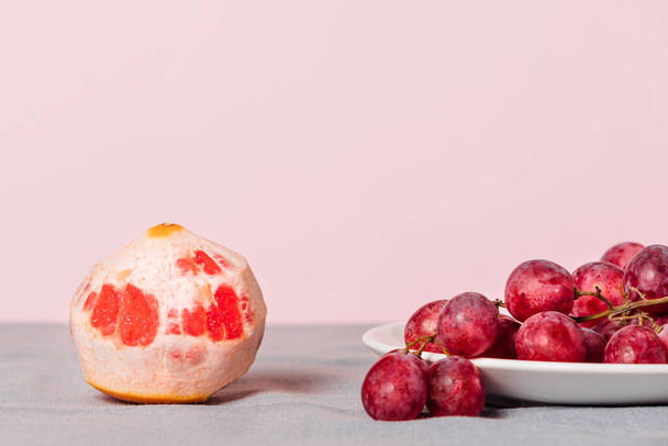 Close-up of a bunch of grapes and a peeled grapefruit on a pink background. Minimalist still life with copy space for your text. - Fotoğraf, Görsel
