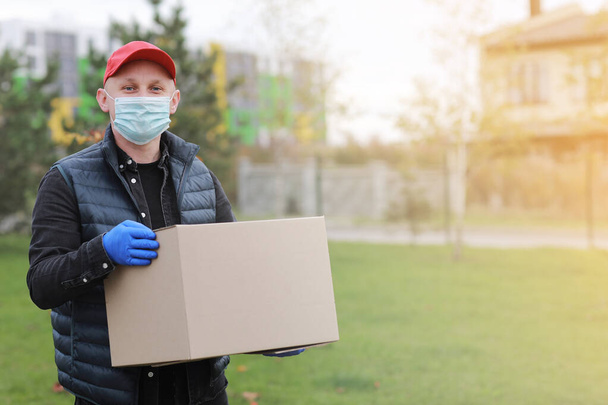 Delivery man in red cap white t-shirt uniform face medical mask gloves hold empty cardboard box on yellow studio background. Service coronavirus. Online shopping. mock up. - Φωτογραφία, εικόνα