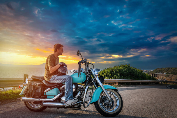 Людина на класичному мотоциклі на краю дороги при заході сонця. - Фото, зображення