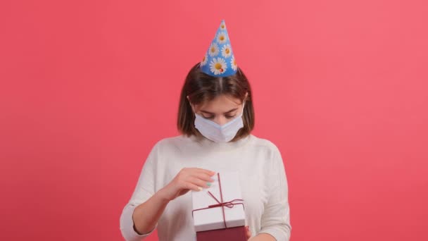Primer plano de una chica optimista con máscara médica en la caja de regalo de apertura de la cara. - Imágenes, Vídeo