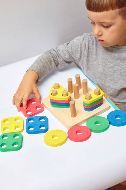 The boy is playing in his room. Learning shapes and colors. A child plays with a sorter. Educational logic toys for kid's. Montessori Games for Child Development. - Фото, изображение
