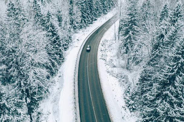 Vue aérienne de la route d'hiver avec une voiture et des arbres enneigés dans la forêt  - Photo, image
