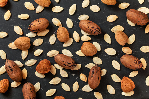 Whole almonds, pecan nuts and pumpkin seeds mixed on black marble like board, view from above - Fotoğraf, Görsel