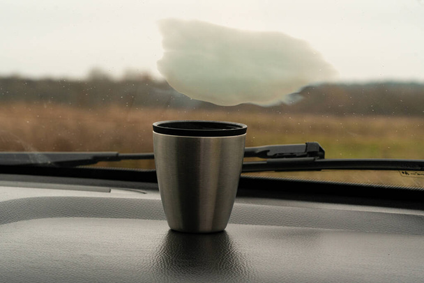 Arabanın torpido gözünde dumanı tüten metal bir fincan kahve. - Fotoğraf, Görsel