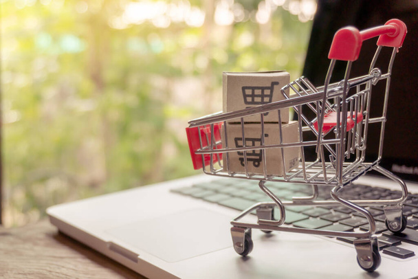 Shopping online concept - Parcel or Paper cartons with a shopping cart logo in a trolley on a laptop keyboard. Shopping service on The online web. offers home delivery - Photo, image