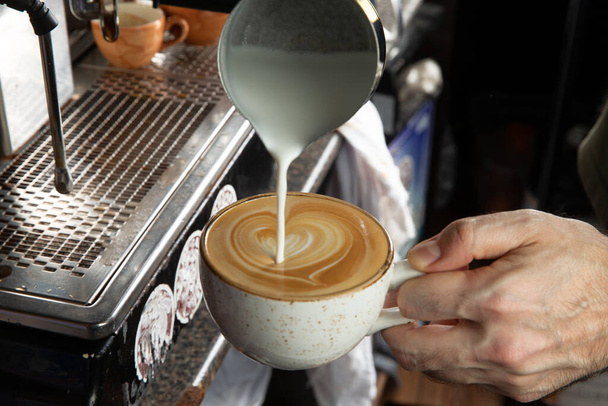 Крупный план мужских рук, наливающих молоко и готовящих свежий капучино, кофе артист и концепция приготовления, утренний кофе - Фото, изображение