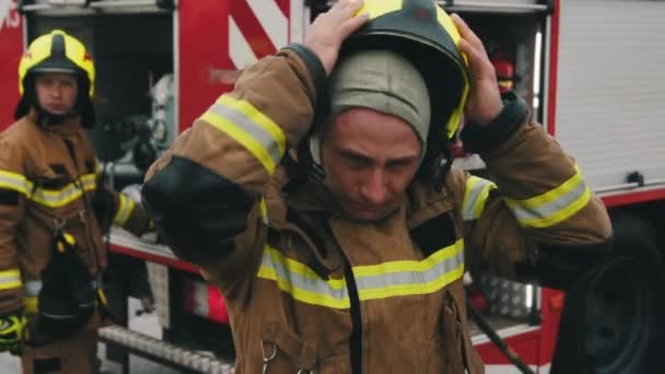A tűzoltó arcképe teljes egyenruhában és a társa a tűzoltókocsi előtt. - Felvétel, videó