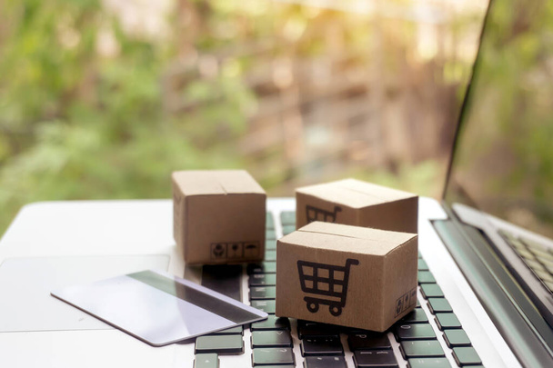 Online nakupování - Papírové krabice nebo balíček s logem nákupního košíku a kreditní kartou na klávesnici notebooku. Nákupní servis na webu a nabízí doručení domů - Fotografie, Obrázek