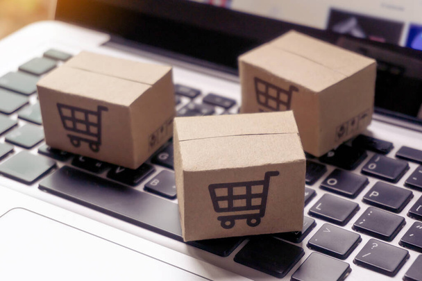 Online-Shopping - Papierkartons oder Pakete mit einem Warenkorb-Logo auf einer Laptop-Tastatur. Shopping-Service im Internet und bietet Lieferung nach Hause. - Foto, Bild