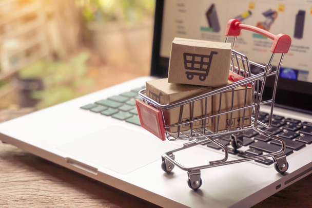 Online vásárlás koncepció - Csomag- vagy papírdobozok bevásárlókosár logóval egy bevásárlókocsiban egy laptop billentyűzetén. Bevásárlási szolgáltatás az interneten. házhozszállítás - Fotó, kép