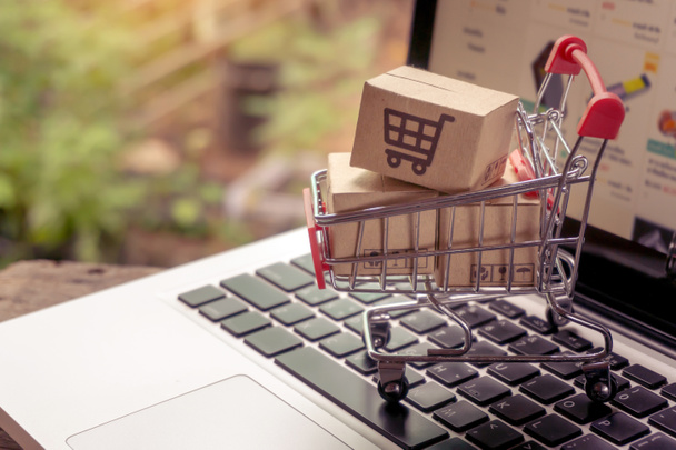 Shopping online concept - Parcel or Paper cartons with a shopping cart logo in a trolley on a laptop keyboard. Shopping service on The online web. offers home delivery - Photo, Image
