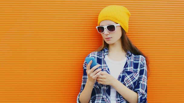Portrait of young woman with phone in the city over colorful orange background - Fotoğraf, Görsel