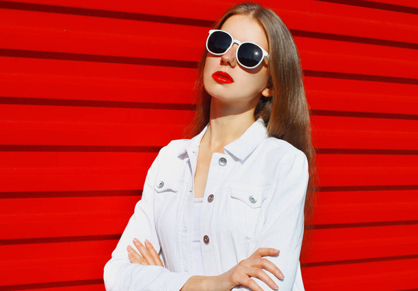 Portrait of young woman wearing a white shirt, sunglasses over a red background - Photo, Image