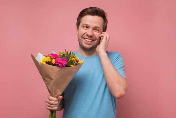 усміхнений чоловік тримає букет квітів, який телефонує своїй дівчині, запрошуючи на побачення
. - Фото, зображення