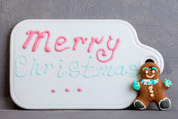 L'iscrizione Buon Natale su una lavagna bianca con crema pasticcera brillante. Un sacchetto di pasticceria con crema di zucchero per decorare un giovane per Natale - Foto, immagini