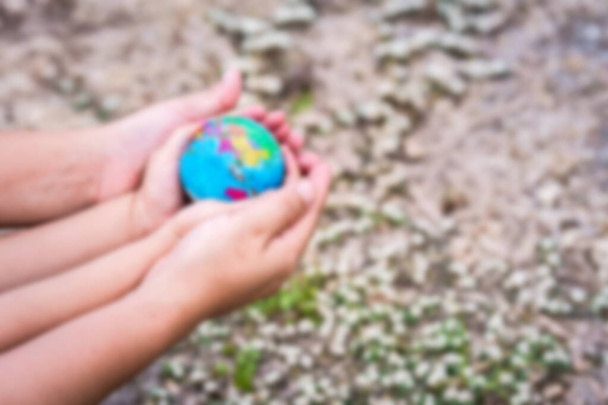 Verschwommene Hände von Mutter und Kind umarmen sich und halten den Globus. Hintergrund ist das Gras. Konzept der Liebe Erde, Welt retten. - Foto, Bild