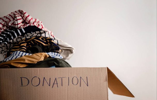 Concepto de donación. Preparación de ropa vieja usada en una caja de donaciones. Enfoque en texto - Foto, Imagen