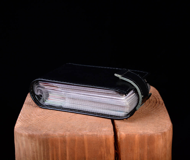 schwarzer Visitenkartenhalter aus Leder auf Holzständer und schwarzem Hintergrund. Kopierraum. - Foto, Bild