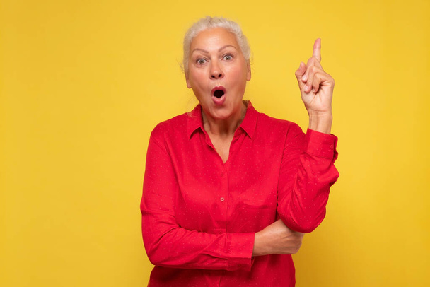 Seniorin zeigt mit erhobenem Zeigefinger und sieht inspiriert von genialem Denken aus - Foto, Bild
