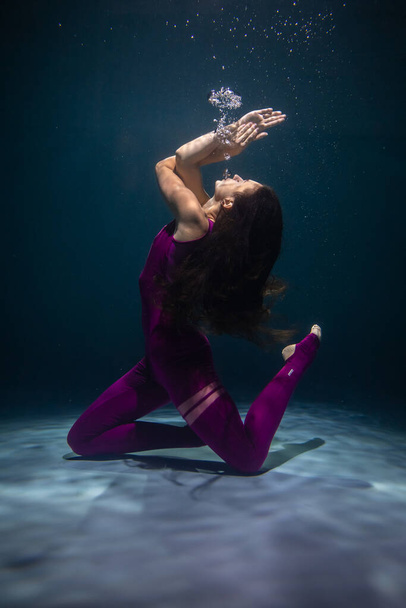 The girl is engaged in yoga under the water in sports clothes. Immersion in Meditation - Fotó, kép