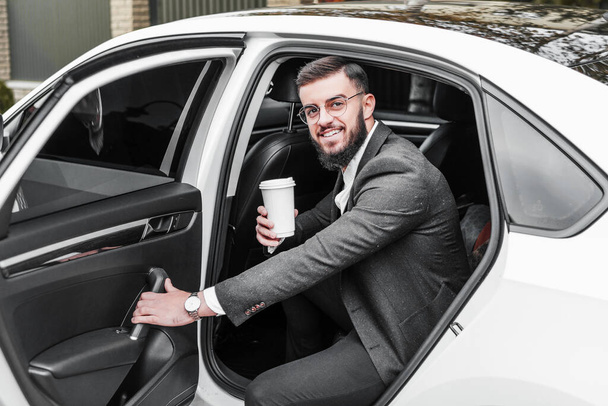 Portrait of a handsome businessman with glasses getting out of his car, smiling and looking at the camera. - 写真・画像