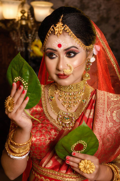 Retrato de novia india muy hermosa sosteniendo hoja de betel, novia bengalí en saree de boda tradicional y maquillaje - Foto, Imagen