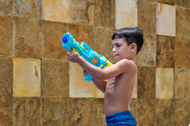 6-leté dítě nabíjení jeho stříkací pistole, kamenná zeď v pozadí. - Fotografie, Obrázek