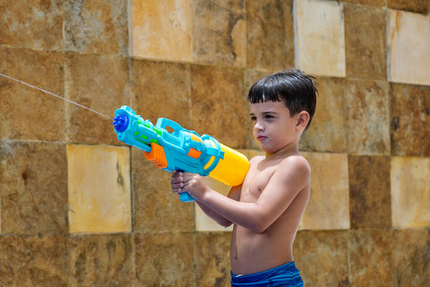 Close-up van een 6-jarig kind schieten met zijn spuitpistool, stenen muur op de achtergrond. - Foto, afbeelding