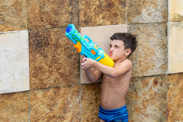 6-jähriges Kind macht ein lustiges Gesicht und schießt seine Spritzpistole in die Luft. - Foto, Bild