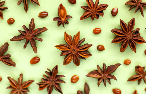 A group of stars anises and seeds isolated on a green background. Flavored asian spices. Flat lay paper card. - Photo, Image