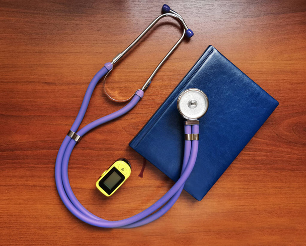 Fioletowy stetoskop, notatnik i przenośny pulsoksymetr na drewnianym tle - Zdjęcie, obraz