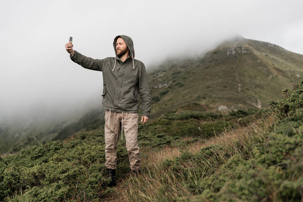 A young traveler stands on the top of the mountain and takes a selfie on a smartphone. Tourism concept. - Foto, imagen