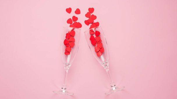 Valentine's day celebration concept. Top above overhead view photo of two champagne flutes filled with red heart shaped confetti isolated on pastel pink background - Photo, Image