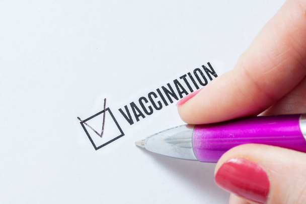 Ο εμβολιασμός αποτελεί θετική απάντηση στο ερωτηματολόγιο. Το χέρι μιας νεαρής γυναίκας γεμίζει τη λίστα ελέγχου και βάζει μια συζήτηση στο θέμα του εμβολιασμού. - Φωτογραφία, εικόνα